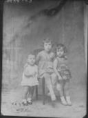 Três crianças um das quais está sentada numa cadeira.