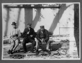 Três civis do sexo masculino sentados num banco de jardim.