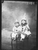 Duas crianças vestidas de Pierrot, sentadas em cima da mesa.