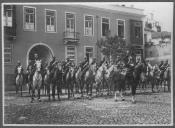 Grupo de militares a cavalo em frente de edifício.